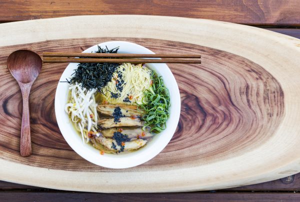 vegan ramen noodle soup for posrpartum sitting on a wooden board with a wooden spoon and chopsticks