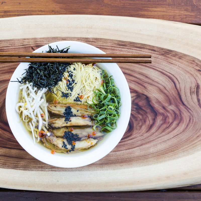 vegan ramen noodle soup for posrpartum sitting on a wooden board with a wooden spoon and chopsticks
